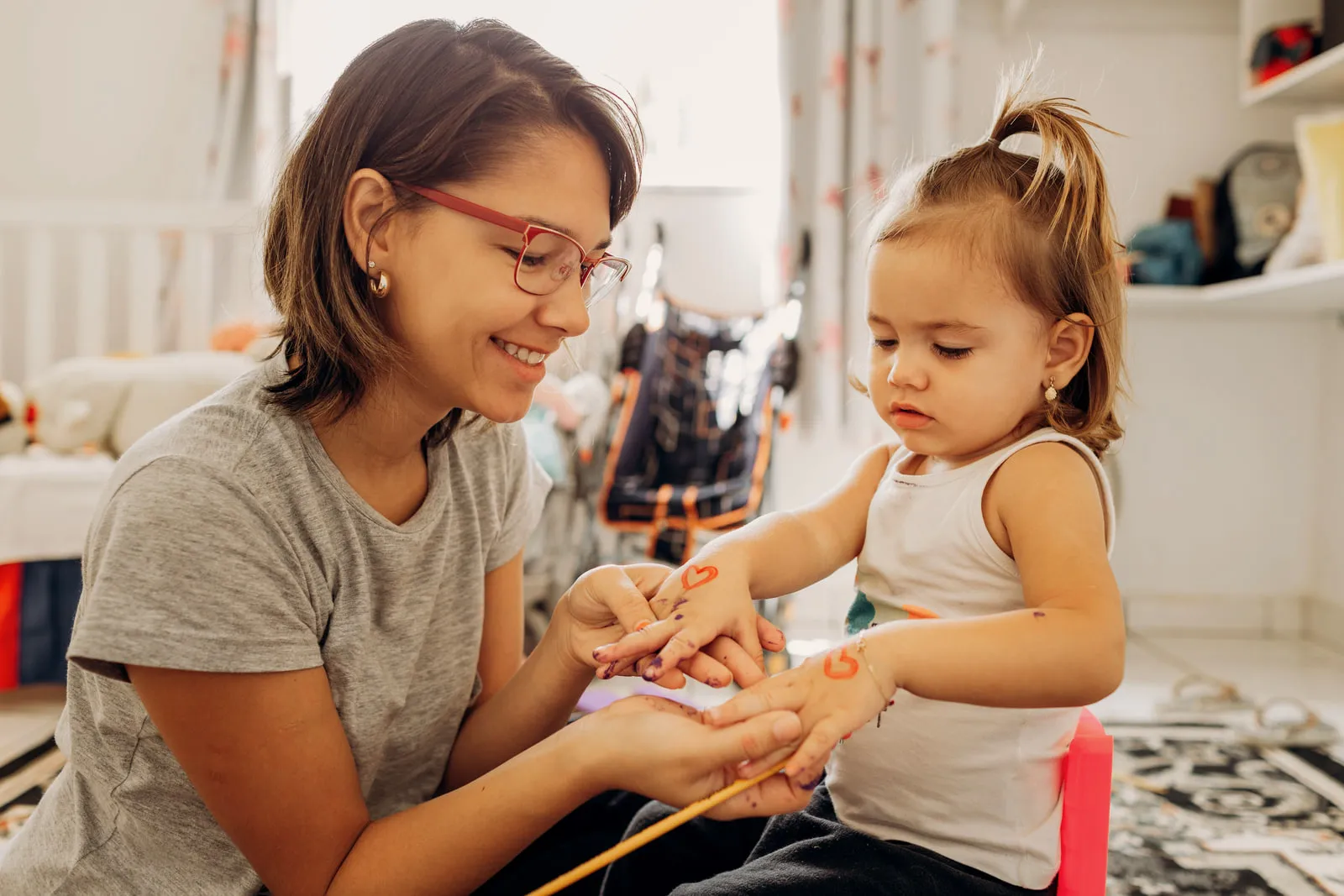 An adult sitting on the floor with a toddler, holding the child’s hands during a play activity.
