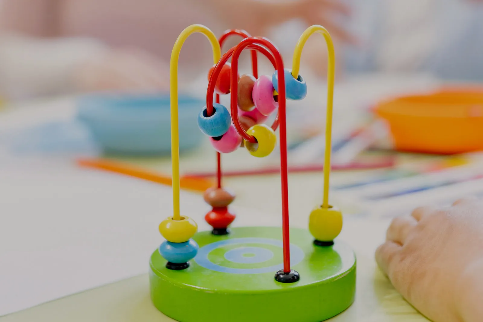 A wooden bead maze on a table in sharp focus, with two children working at the table out of focus behind it.